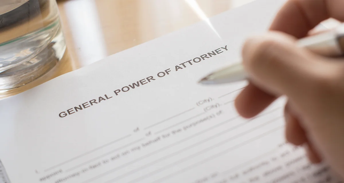 Hand signing a General Power of Attorney document with a pen on a desk.