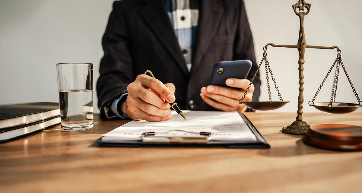 Professional consultant reviewing documents and using a smartphone beside legal scales, representing Legal Translation Service support for official documentation and business communication.