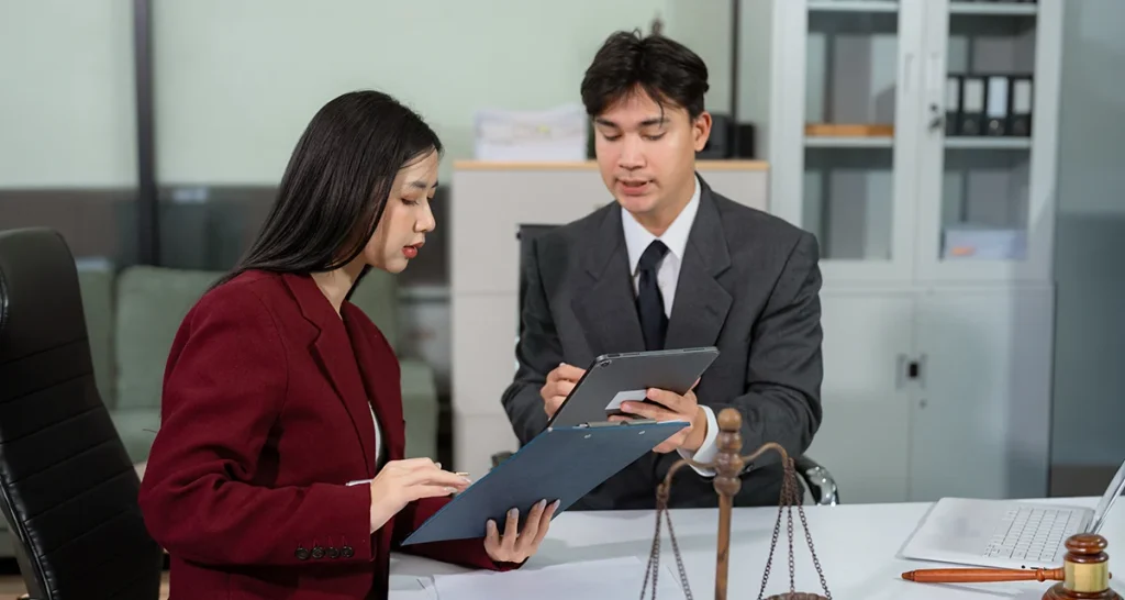 Two legal professionals discussing and reviewing legal documents on a tablet and clipboard in an office setting to ensure Power of Attorney Dubai validity.
