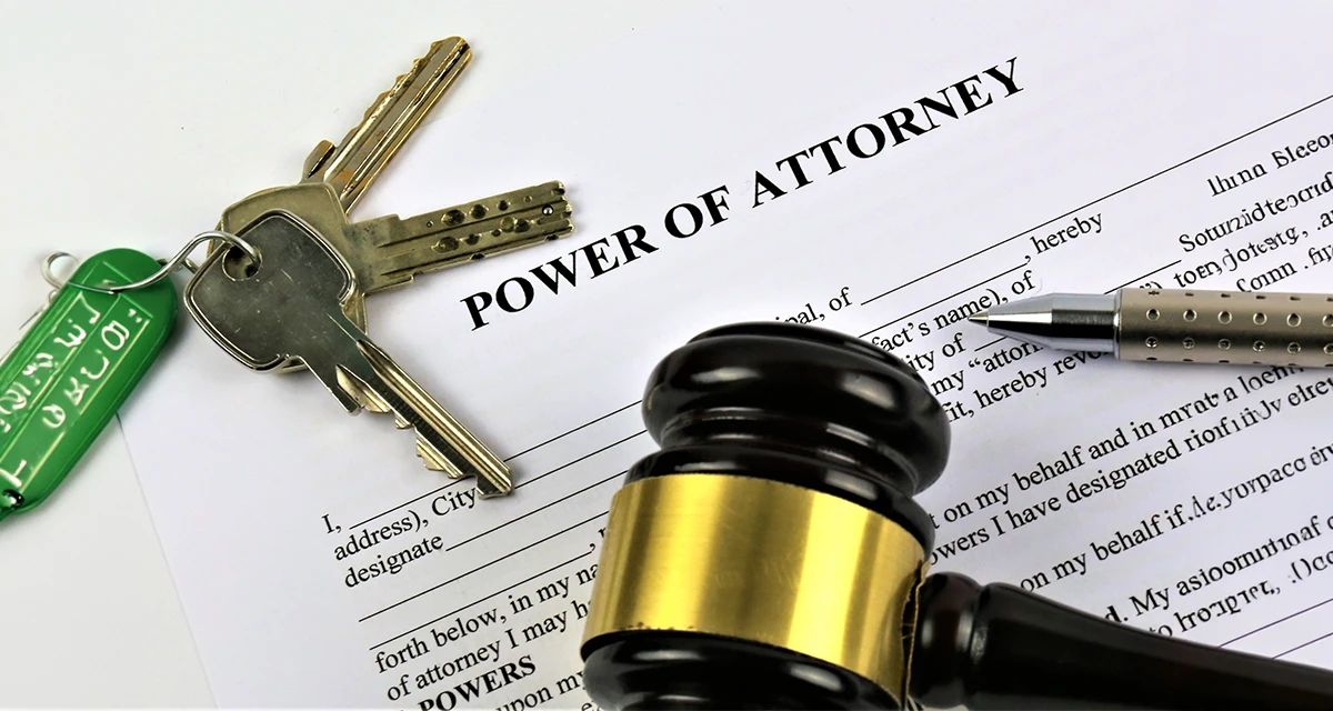 A legal document titled "Power of Attorney" lying on a white surface, accompanied by a set of house keys, a silver pen, and a wooden judge's gavel, representing the process of granting a personal power of attorney in Dubai.